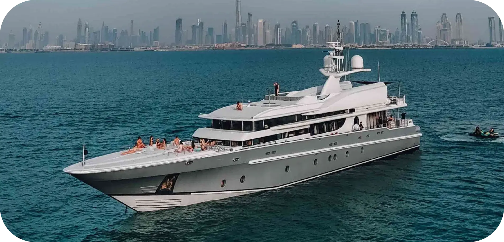 Side view of Big Boaty, a grey-hulled Oceanfast superyacht, under way off Dubai with guests on the foredeck and a jet ski astern