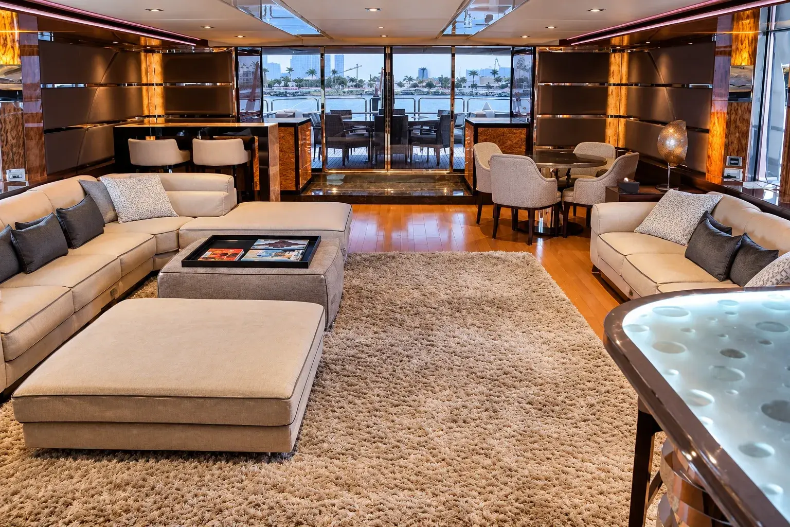 Illustration of the Big Daddy main saloon, with cream sofas, a deep-pile rug, burl-wood panels and glass doors open to the aft deck