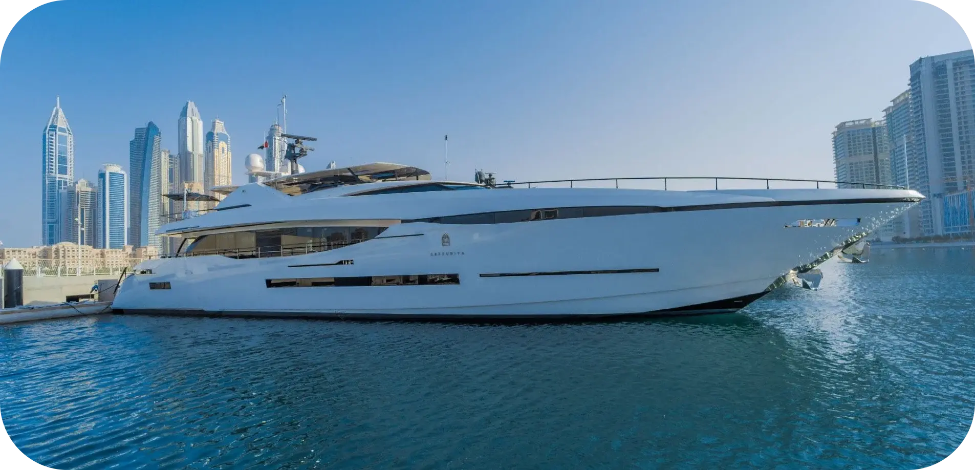 Side view of Bridgetown, a white 124 ft Peri yacht with long dark window bands, moored in front of high-rise towers