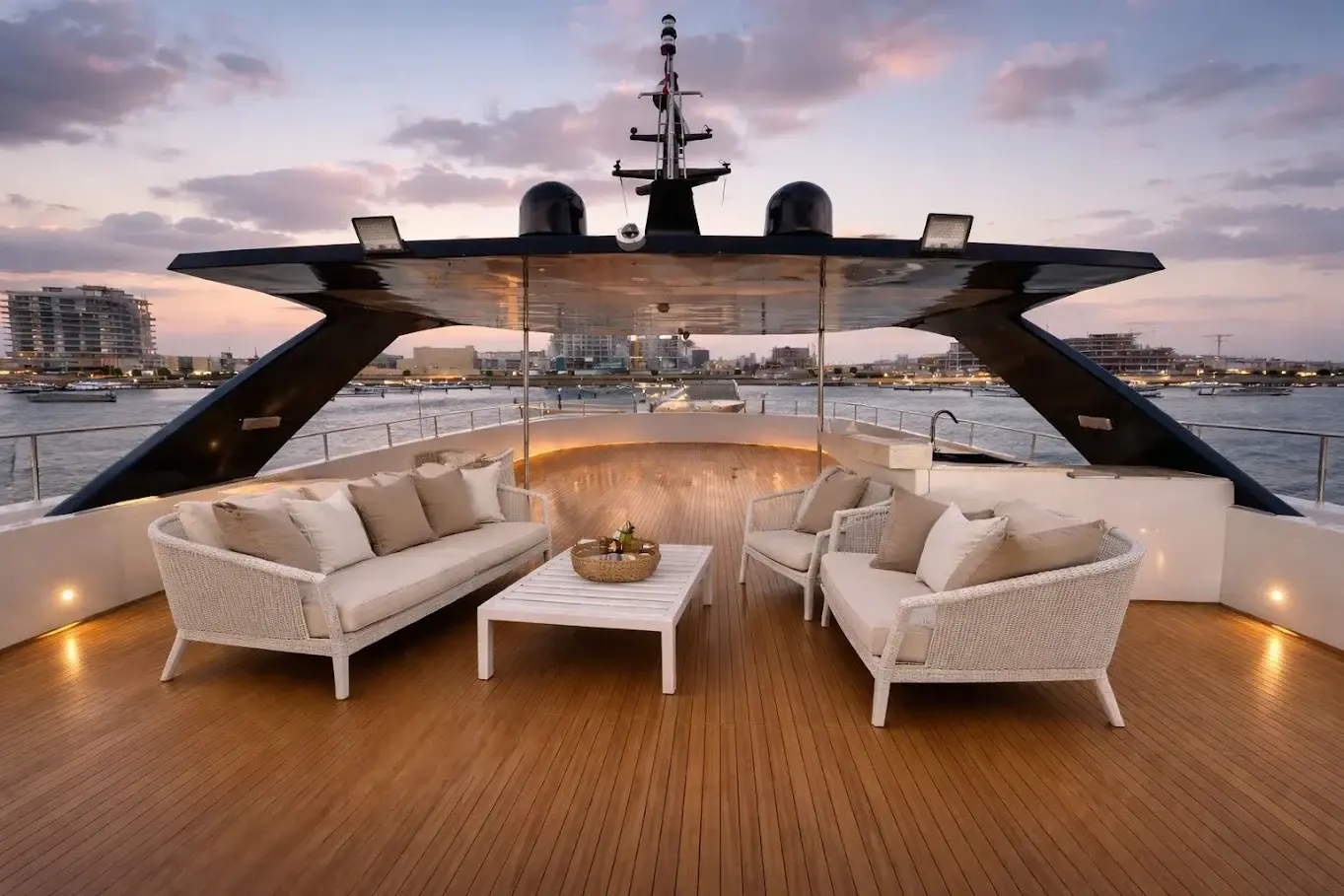 Carmen top deck at sunset, with white wicker sofas on teak under a black hardtop and the marina behind