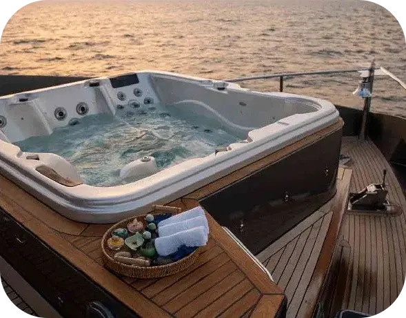 Eclipse deck Jacuzzi on a teak deck at sunset, with a basket of rolled towels beside it and the sea behind