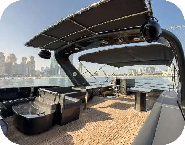 Grey Beast flybridge with dark sofas and pedestal tables on a teak deck under a black hardtop, a city skyline across the water