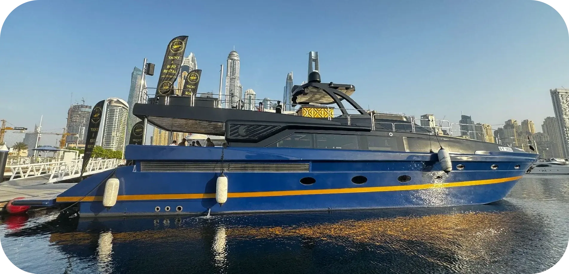 Side view of I Don't Know, a 95 ft Gulf Craft with a deep blue hull, an amber stripe and a charcoal superstructure, moored against the Dubai skyline