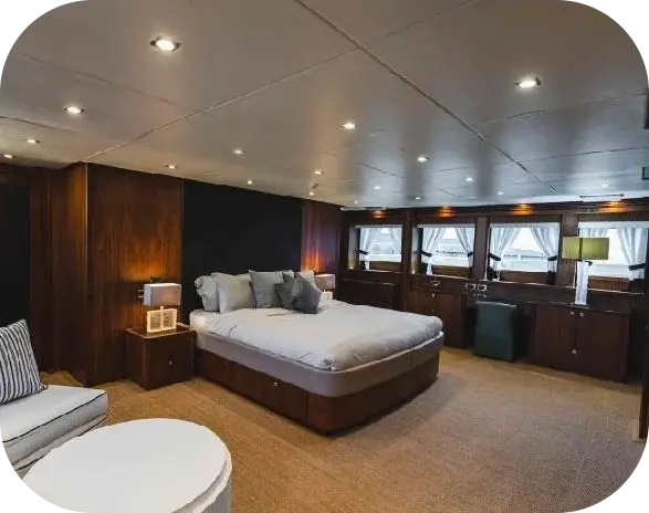 Liquid Asset cabin with a large double bed, dark timber panelling, a dressing table and a row of curtained windows