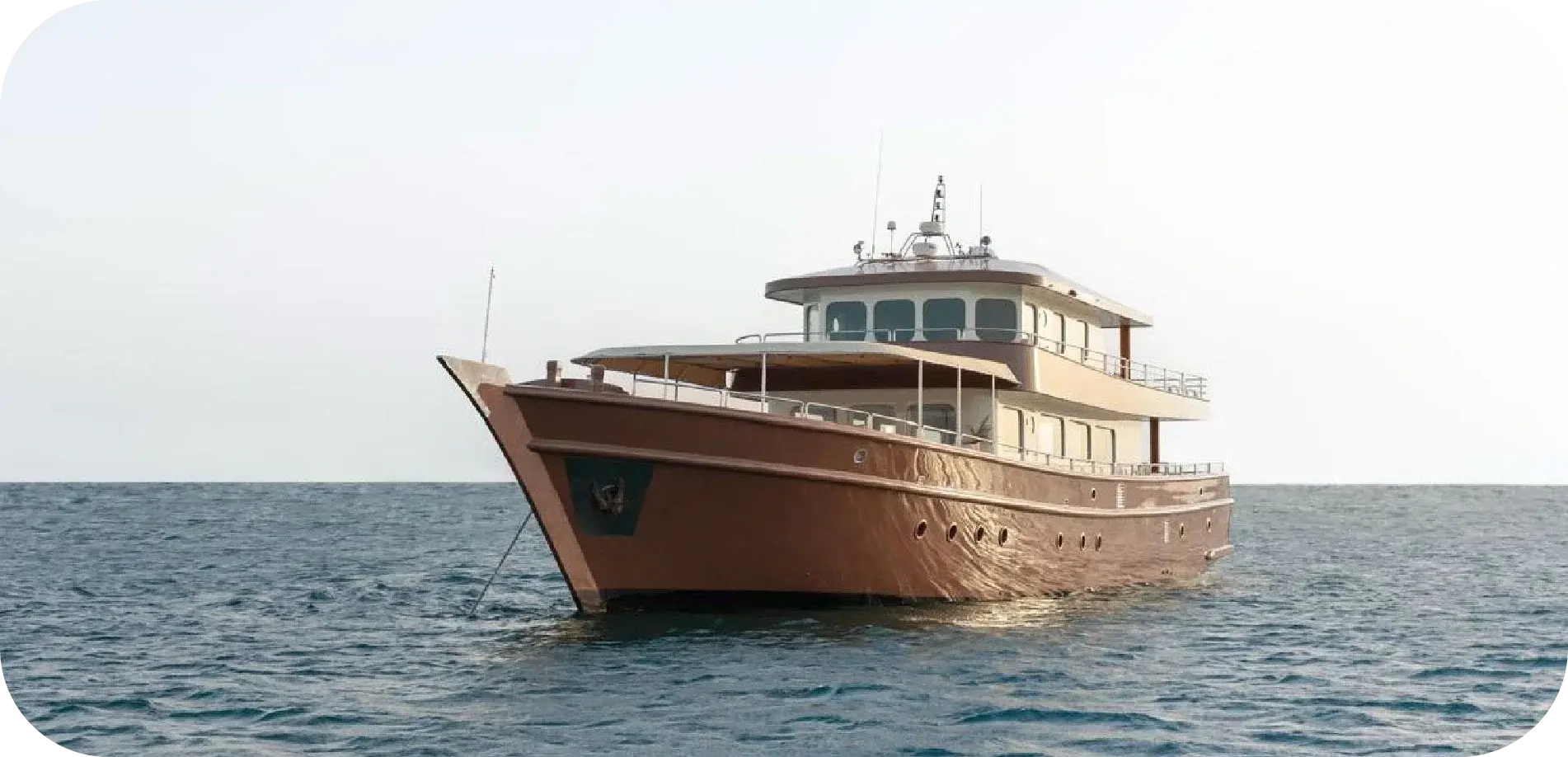 Side view of Melody 2 at anchor, with a copper-coloured hull, a raked bow, an awning over the foredeck and a wheelhouse above