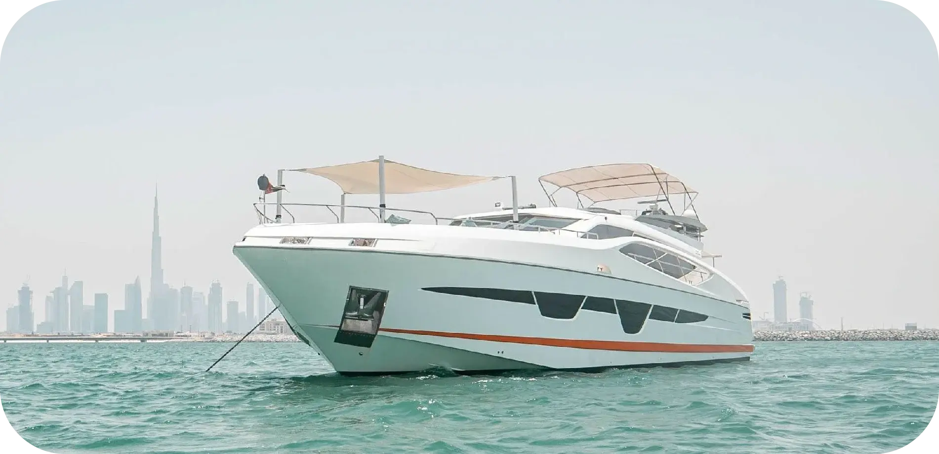 Bow view of Out of Office, a white Numarine 105HT with angled hull windows, an orange waterline stripe and a shade sail over the bow, at anchor off Dubai