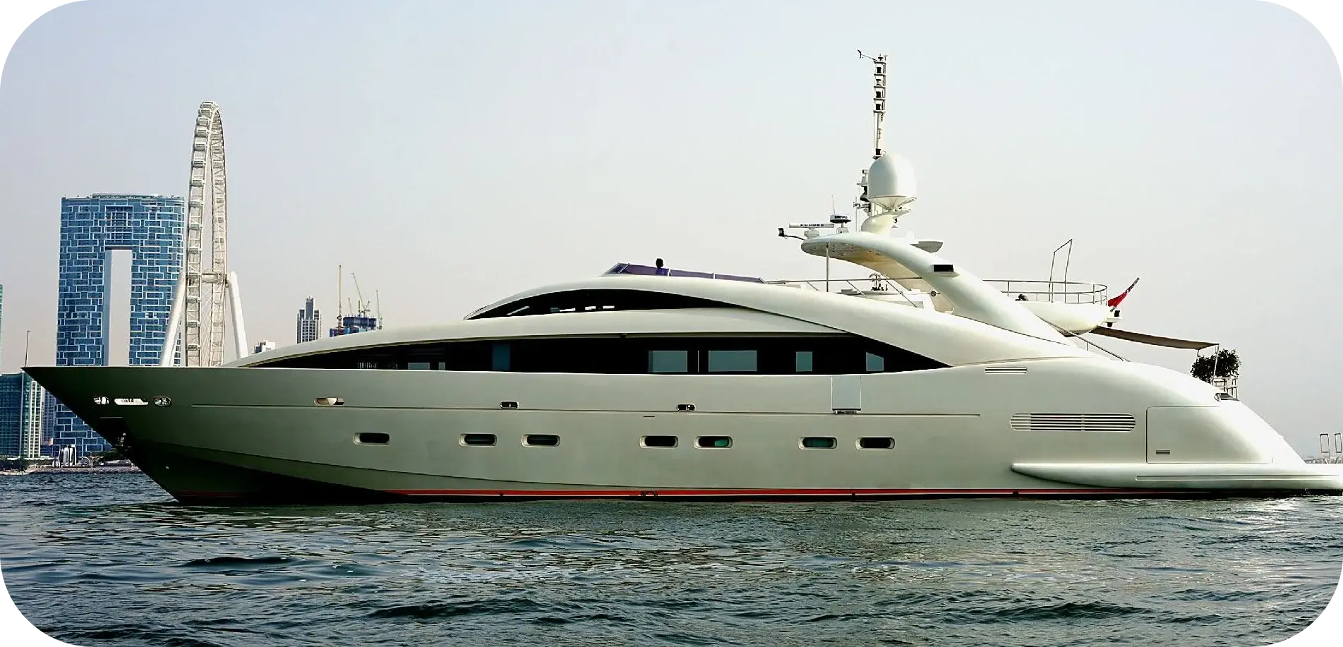 Side view of Royal Freedom, a pale ISA motor yacht with a dark band of windows and a curved arch, at sea off Dubai with the Bluewaters observation wheel behind