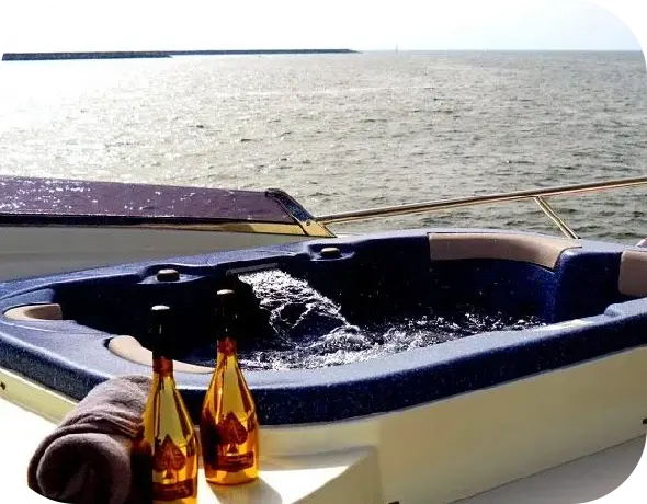 A jacuzzi on the deck of Royal Freedom, with two gold bottles and a folded towel on its edge and open sea beyond