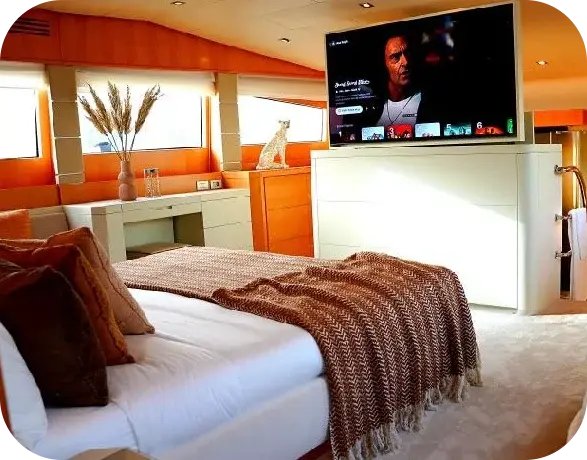 Royal Freedom guest cabin with a double bed, a brown woven throw, wood panelling and a television on a white cabinet at the foot of the bed