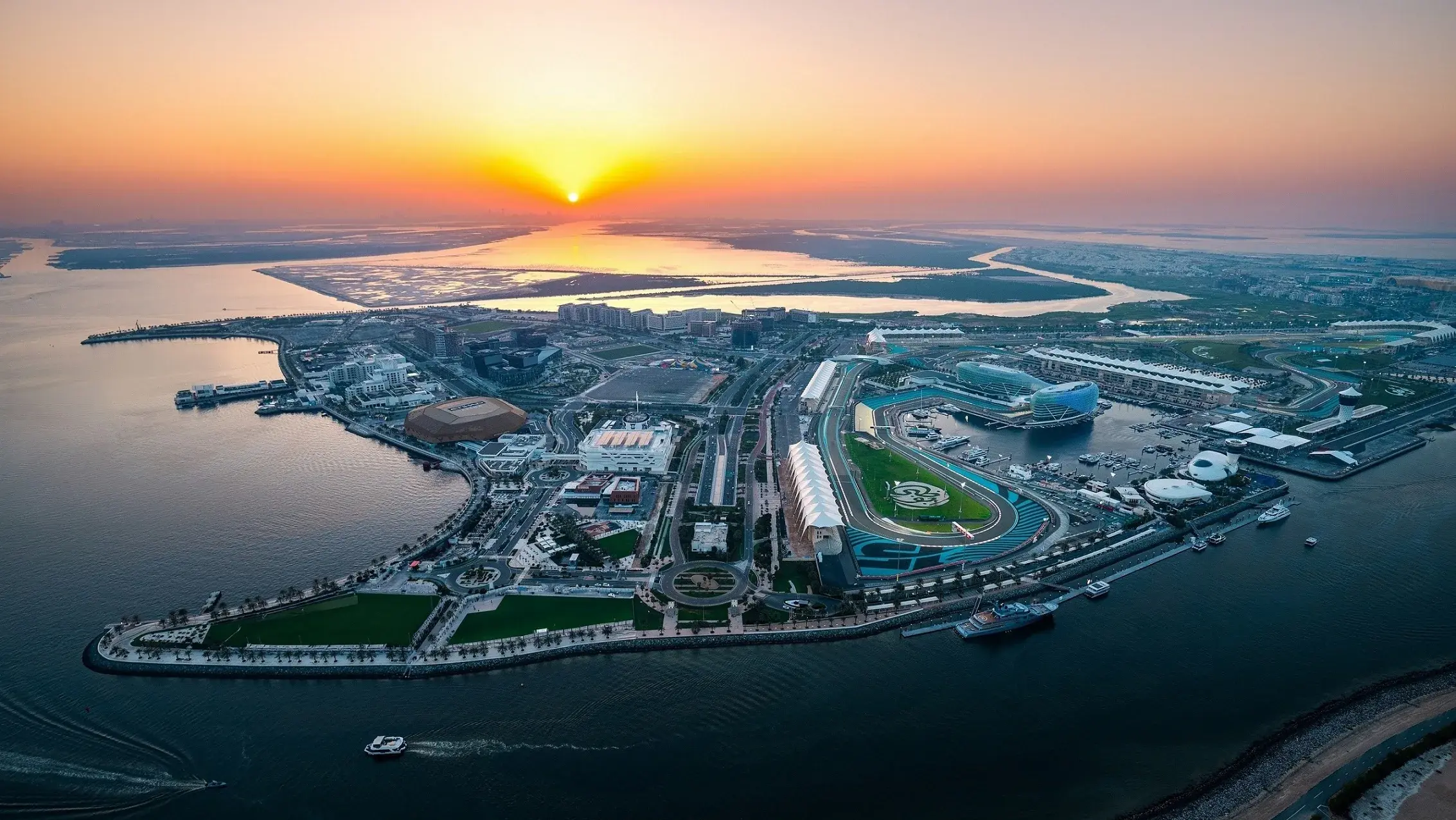 Yas Island from above at sunset, with Yas Marina Circuit looping around the marina and yachts moored beside the track