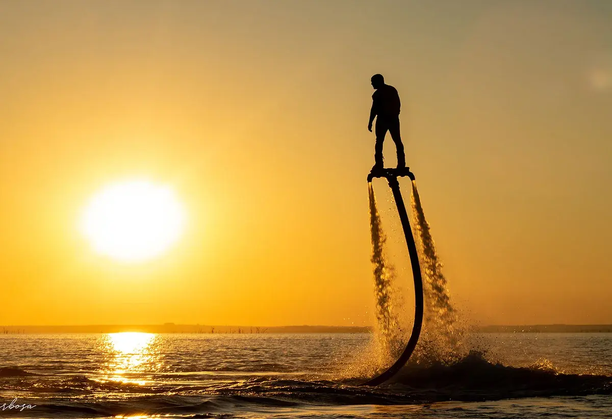 A flyboard rider lifting above the sea at sunset