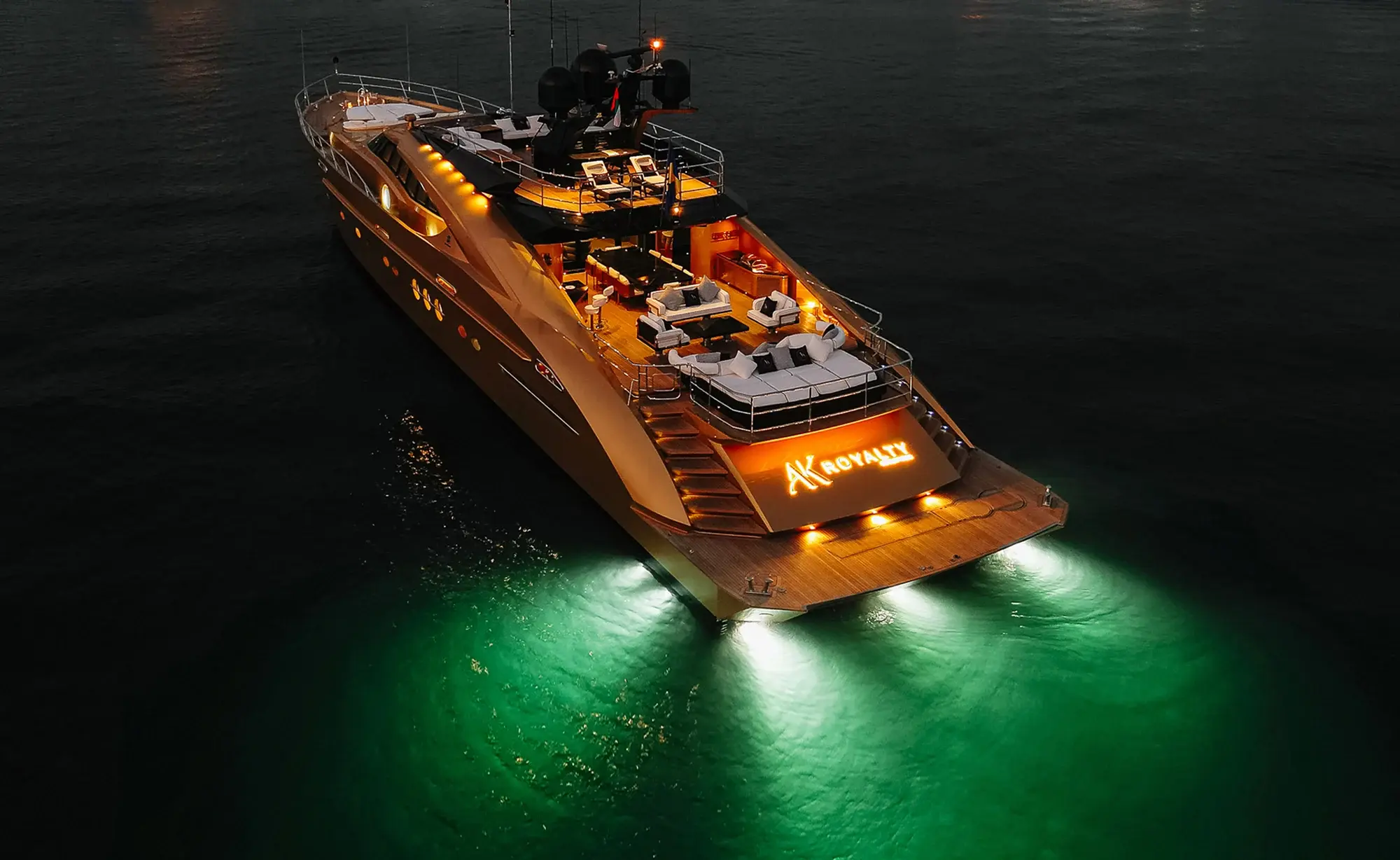 AK Royalty lit up at night, its gold hull reflecting on the water