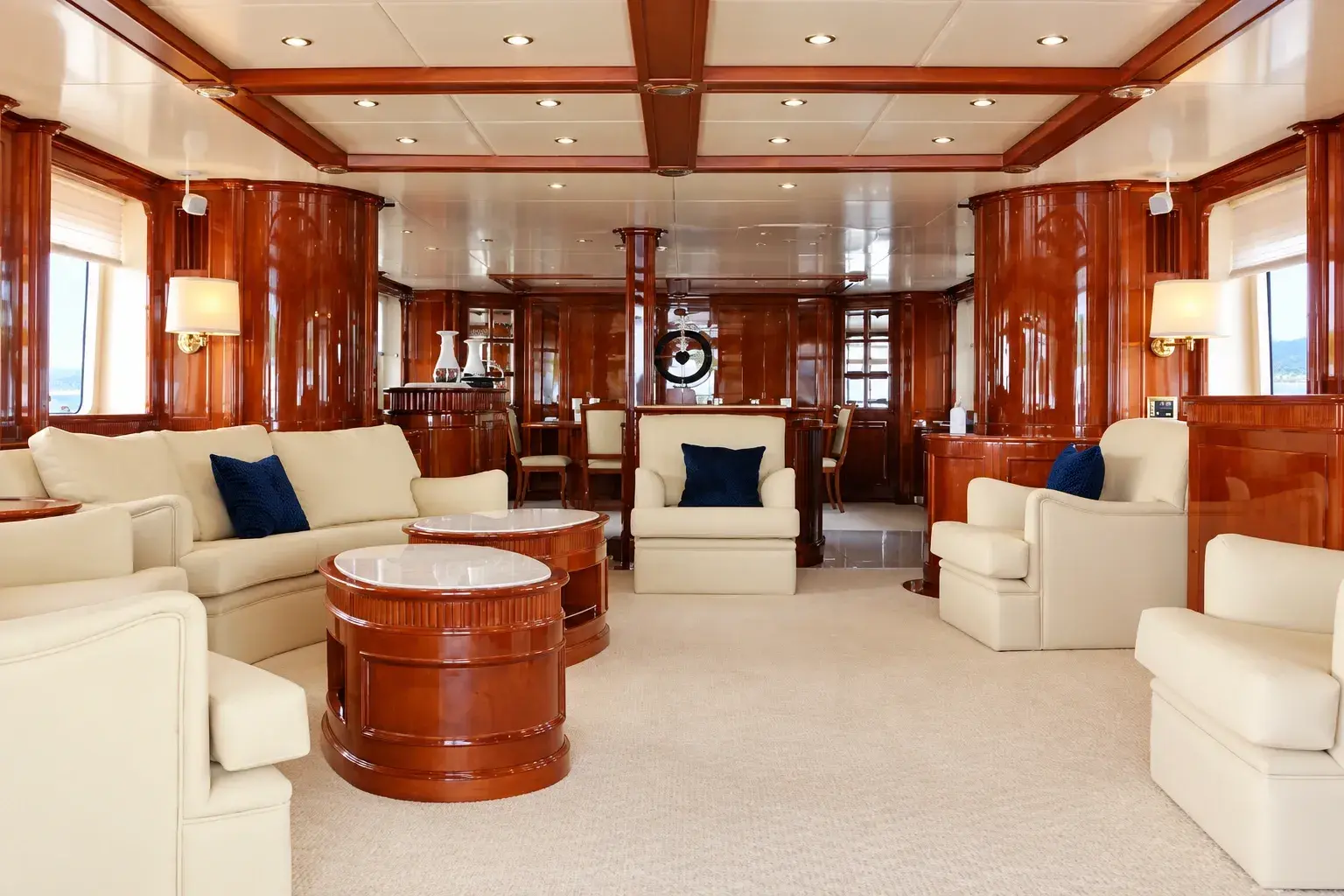 Illustration of the Island Girl 2 saloon, with glossy timber panelling, cream sofas and armchairs, round marble-topped tables and a dining table beyond